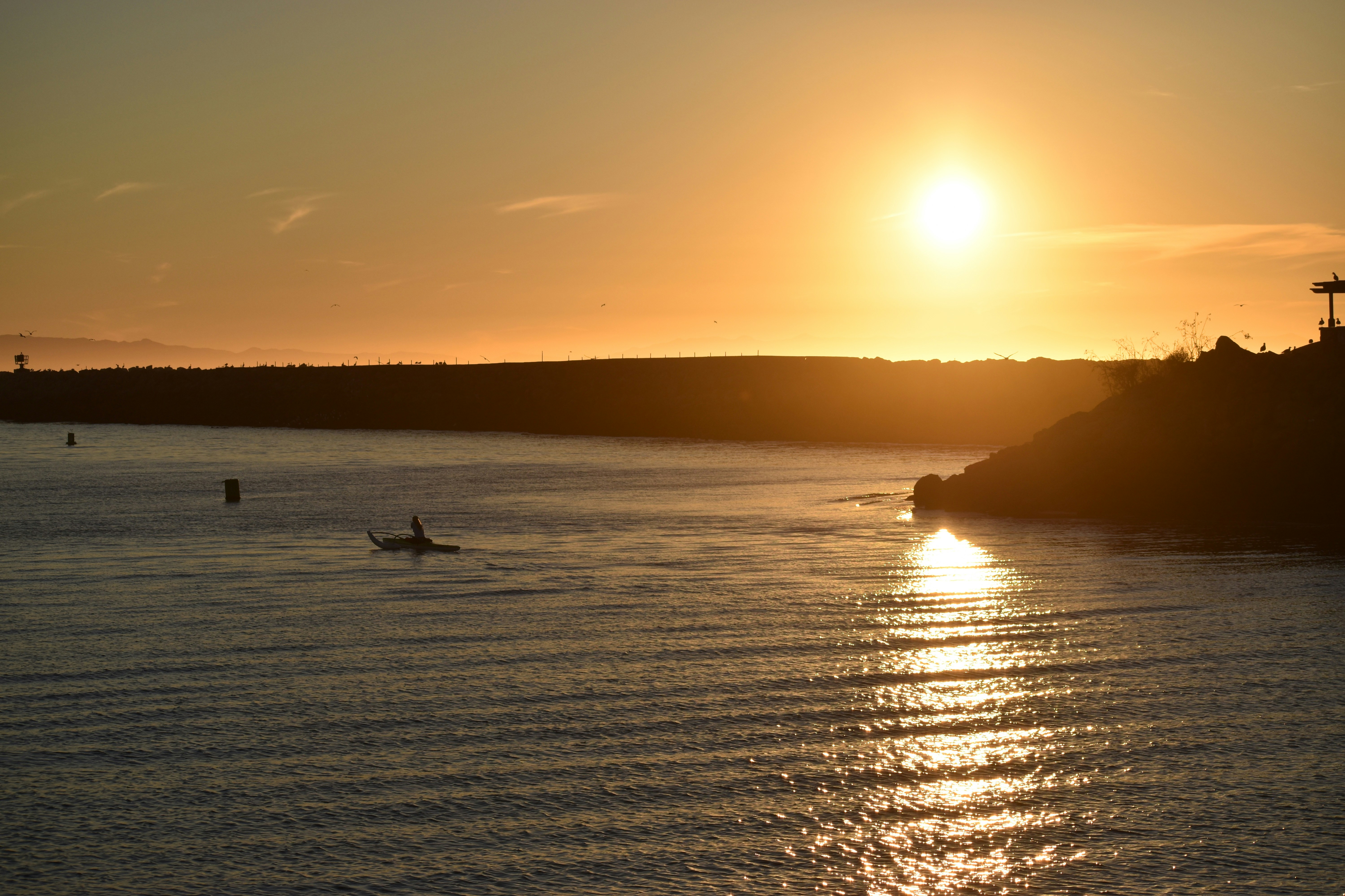 Kayaker on calm lake at sunset, warm golden light, peaceful water surface