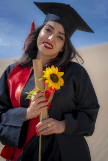 a woman in a graduation gown holding a sunflower