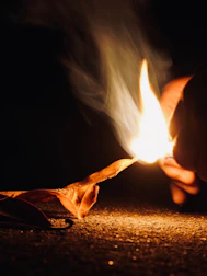 Hands skillfully striking flint to spark a primitive fire amid autumn leaves.