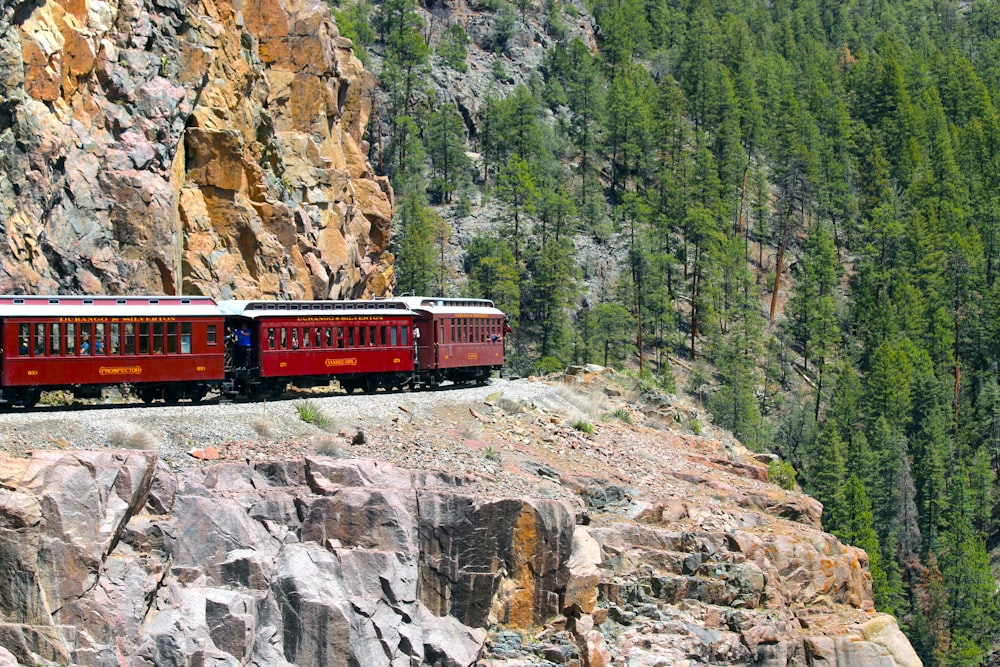 a red train traveling down train tracks next to a mountain