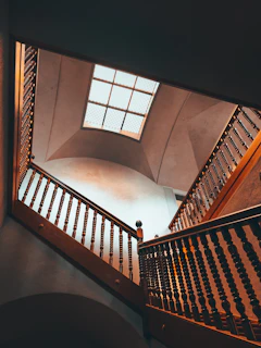 Interior view of a high-end residential stairwell with a double-height family room and natural light pouring through a large skylight.