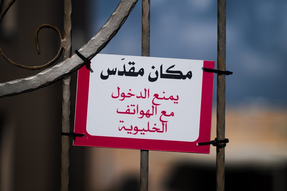 a red and white sign hanging on a metal fence
