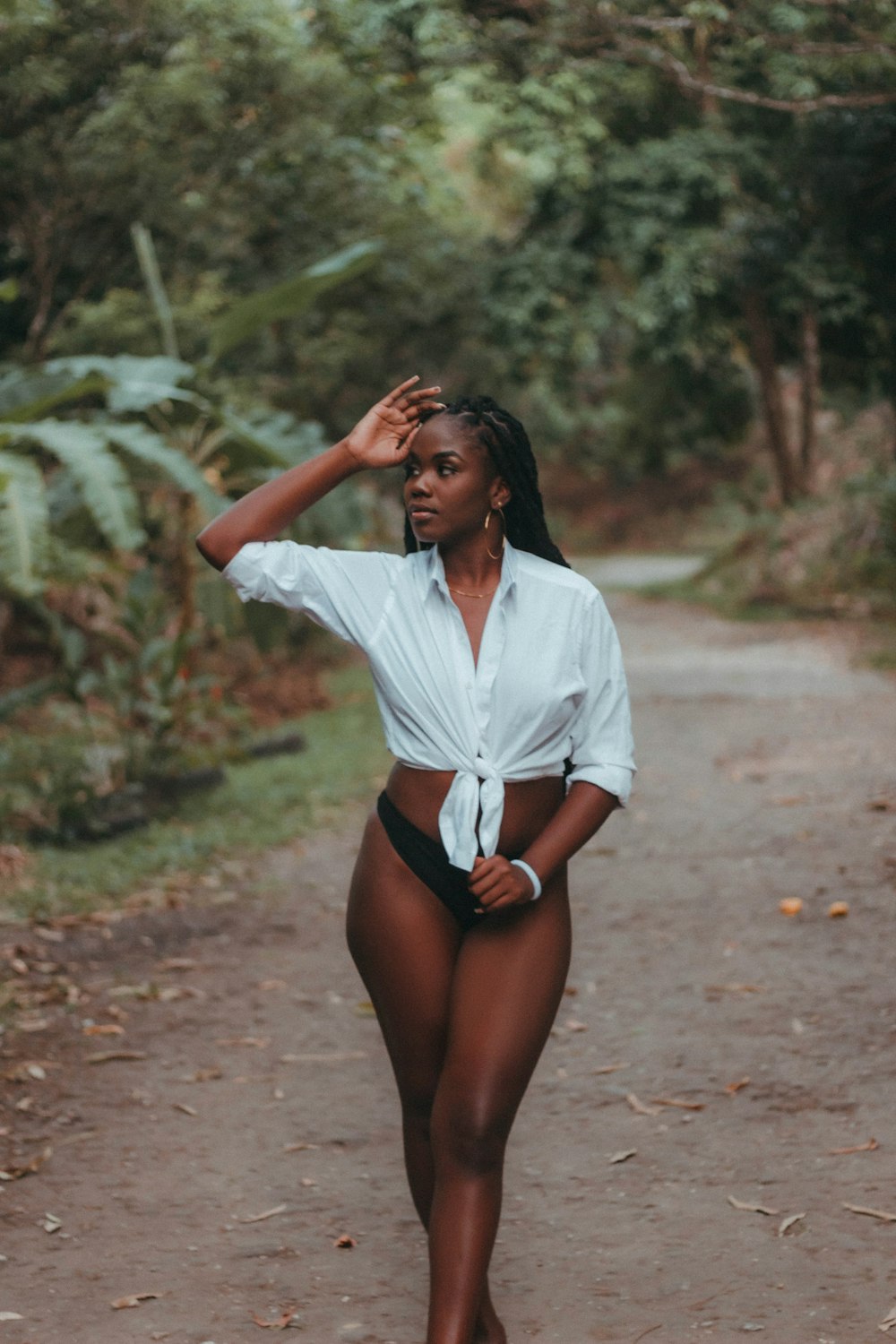 a woman in a white shirt and black panties walking down a dirt road