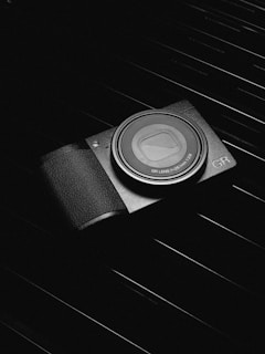 A compact camera with a textured grip and a visible lens is placed on a dark, ribbed surface. The camera