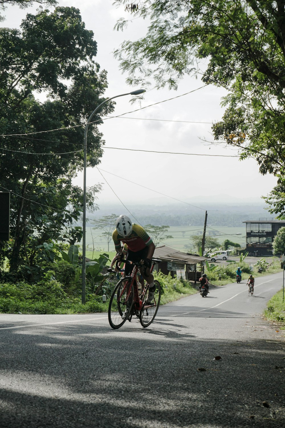 a man riding a bike down a street next to a lush green hillside