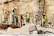 Workers wearing safety gear are engaged in construction activities at a site with rocky terrain. They are handling large metal rods, possibly for reinforcing concrete structures. Piles of earth and construction materials surround the area.