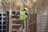 A construction worker wearing a yellow safety vest, blue sweater, and yellow hard hat is seen working among steel bars. The worker appears to be assembling or inspecting a structure made of metal and concrete.
