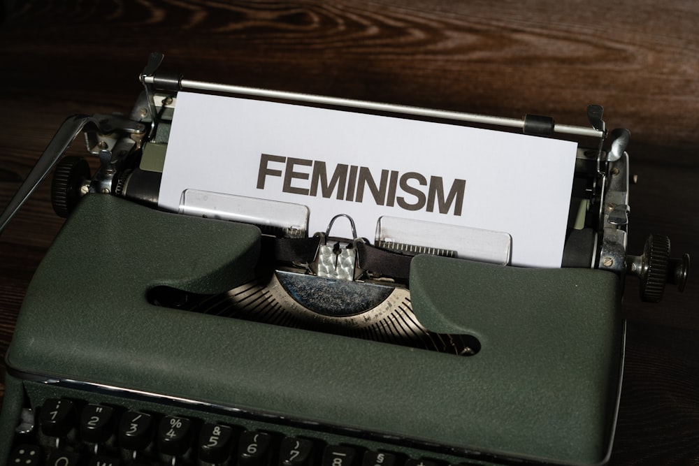 a close up of a typewriter with a paper that reads feminist