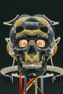 A futuristic, stylized robotic skull with glowing eyes and intricate designs is featured. The structure includes metallic and reflective surfaces, with neon lights outlining parts of the skull. The colors are predominantly dark with accents of yellow and red, creating a mechanical and sci-fi aesthetic.