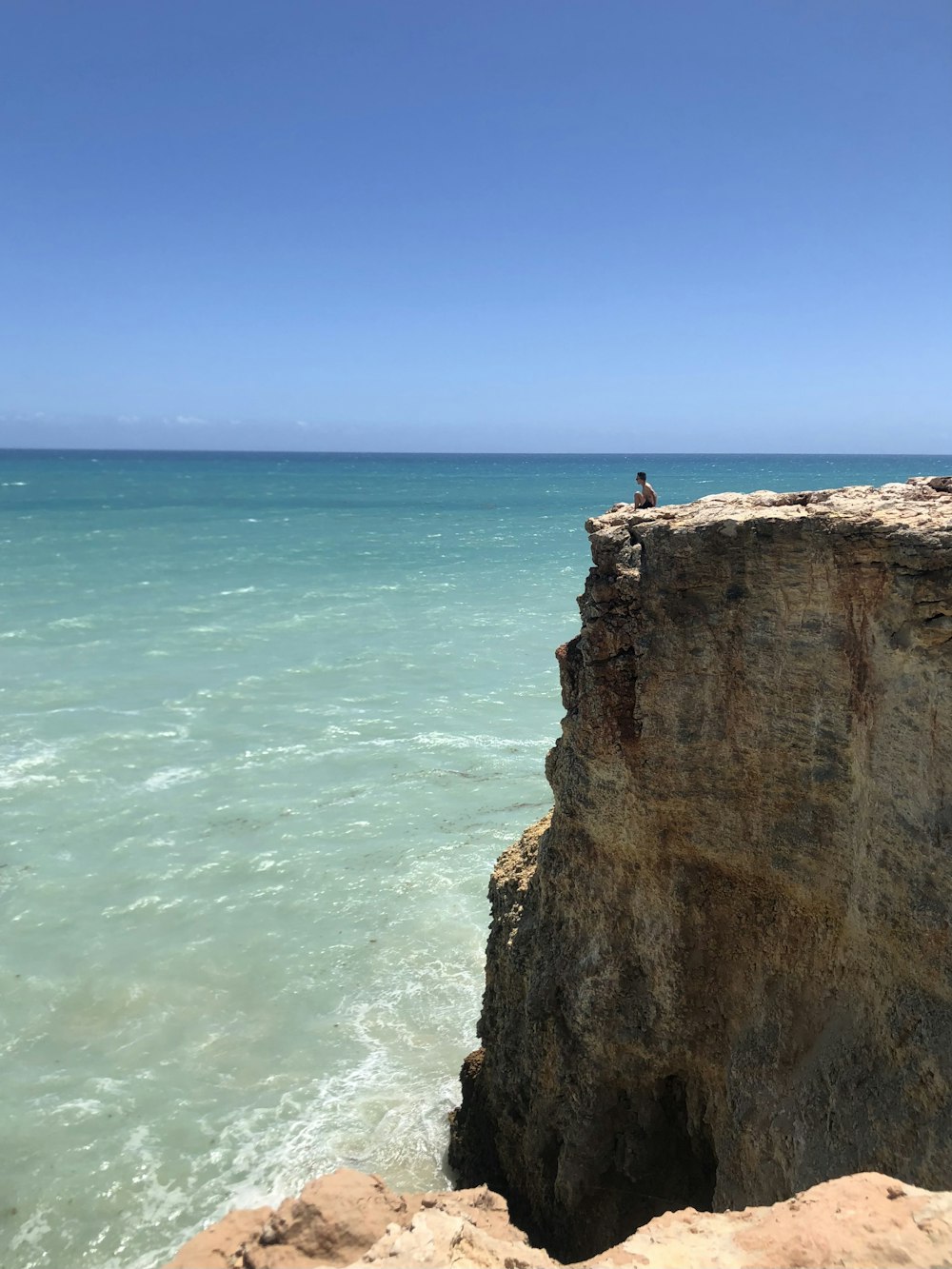 Una persona sentada en un acantilado con vistas al océano