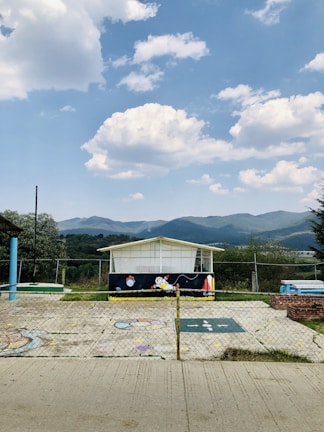a fenced in area with a building and mountains in the background
