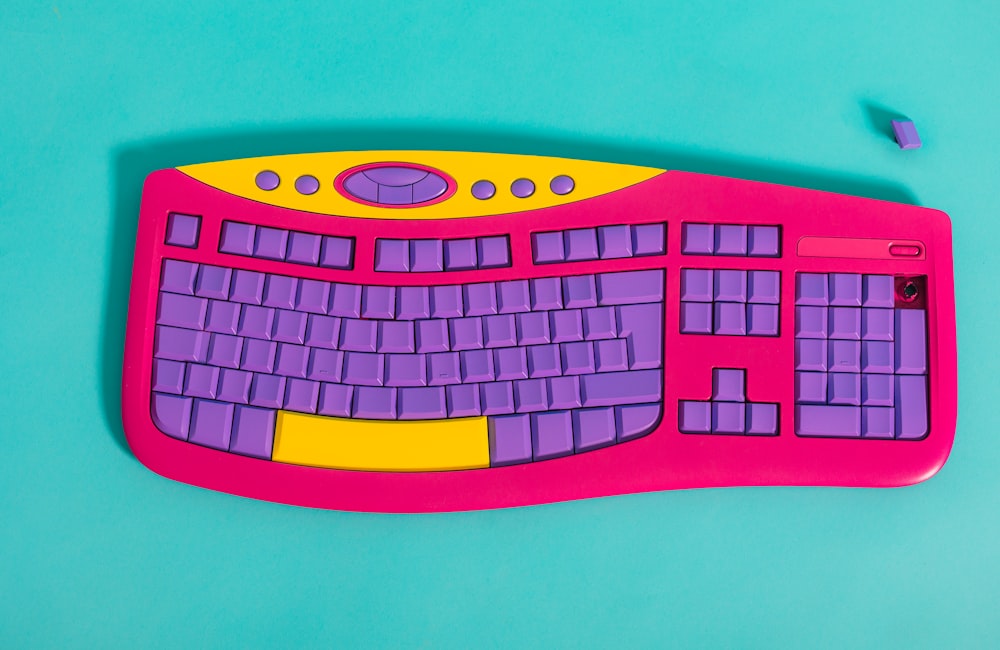 Un teclado rosa y amarillo sentado encima de una superficie azul
