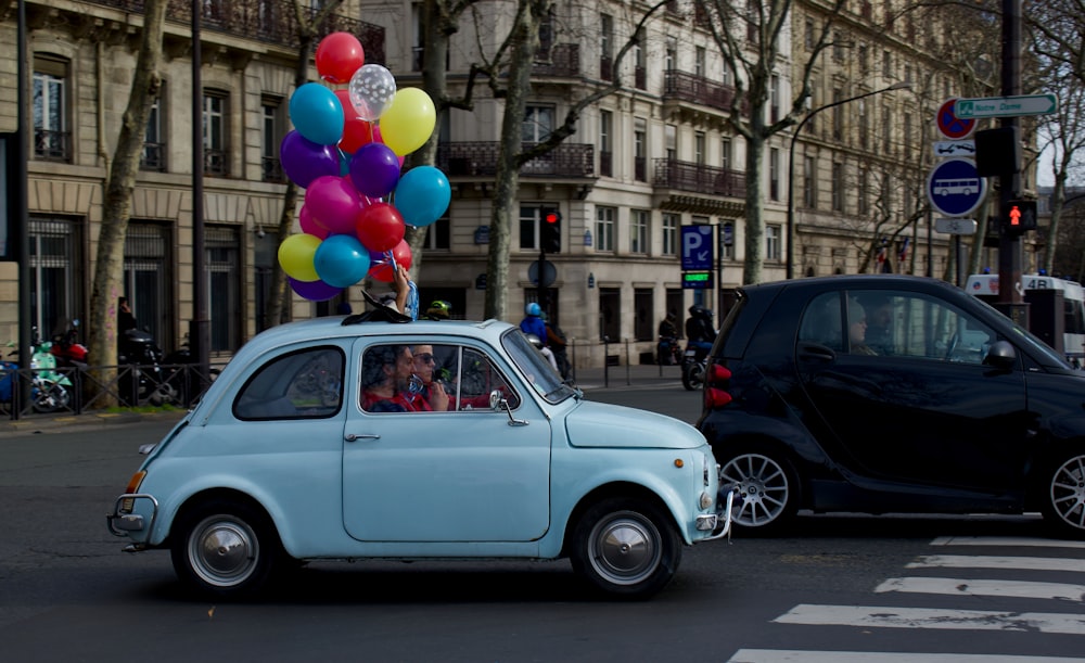 a small blue car driving down a street next to a black car