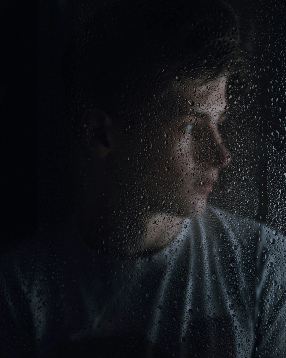Ein Mann steht vor einem vom Regen bedeckten Fenster