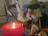A wooden figurine holding a staff and dressed in a green cloak stands next to a burning red candle. The smoke from the candle swirls in the air, adding a mystical feel to the scene. The figurine has a detailed mustache and beard, made from light-colored fibers, and wears a green hat. The background is softly out of focus, drawing attention to the foreground elements.