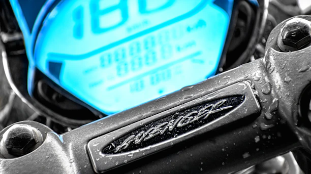 A close-up shot of a sleek motorcycle dashboard with city lights blurred in the background.