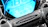 A close-up shot of a sleek motorcycle dashboard illuminated in neon blue against a dark background.