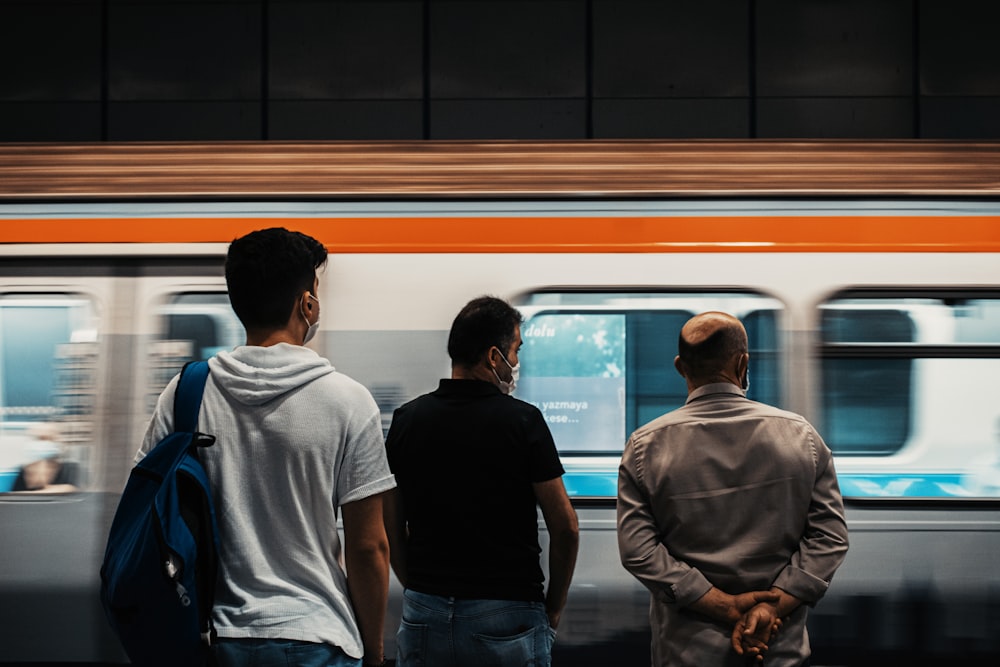 three men standing in front of a subway train