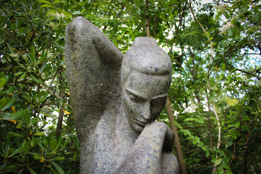 a statue of an angel sitting in the middle of a forest