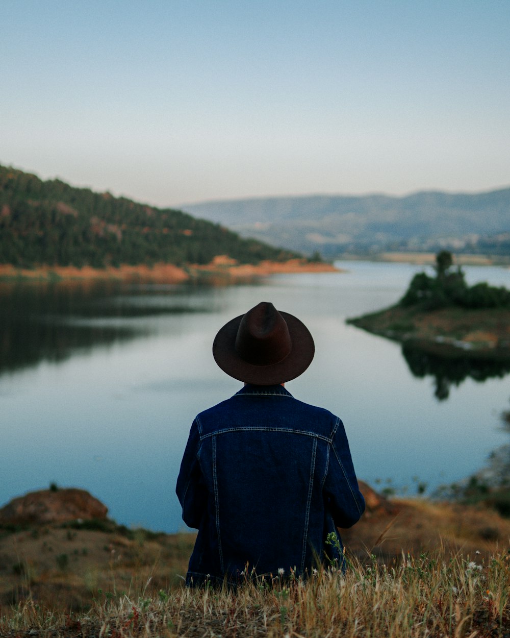 a man wearing a cowboy hat looking out over a lake