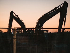 the silhouette of a construction vehicle behind a fence