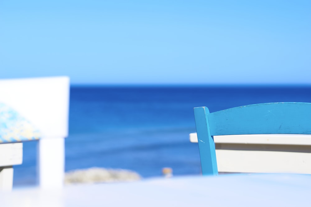 a white table with a blue chair next to the ocean