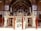 An intricately designed throne or platform is supported by several carved marble figures in an ornate room. The room features an abundance of mirror work and ornate patterns on the walls and archways. A red rope barrier surrounds the central structure.