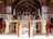 An intricately designed throne or platform is supported by several carved marble figures in an ornate room. The room features an abundance of mirror work and ornate patterns on the walls and archways. A red rope barrier surrounds the central structure.