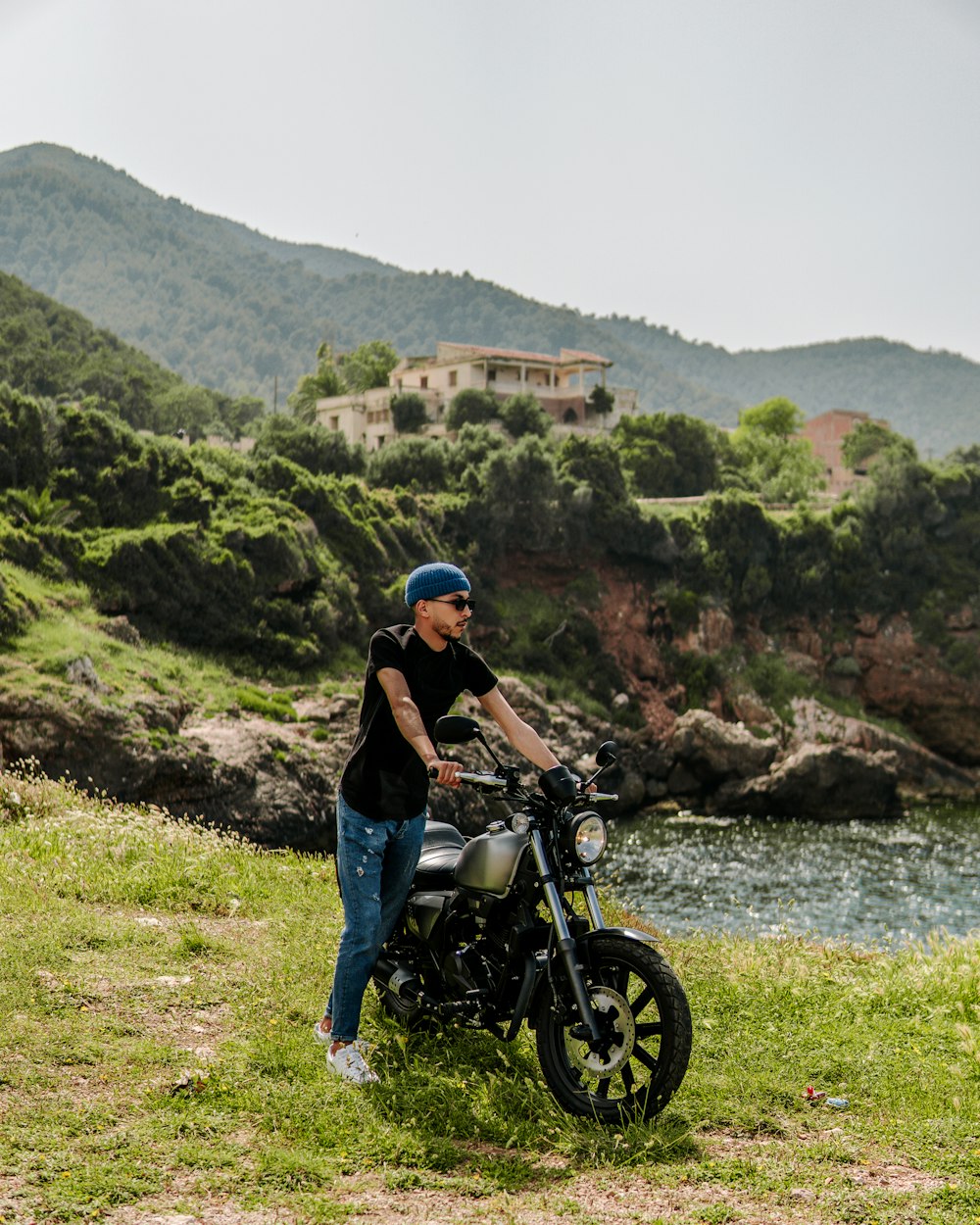 a man standing next to a motorcycle on a lush green hillside