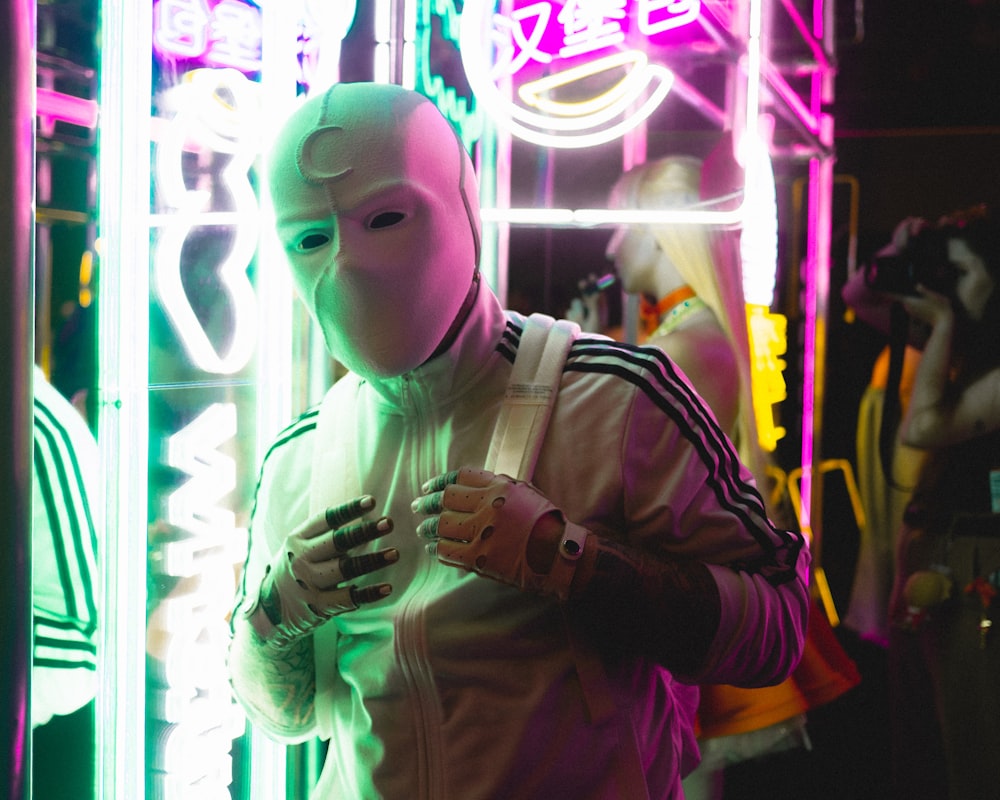 a person wearing a white mask standing in front of neon signs
