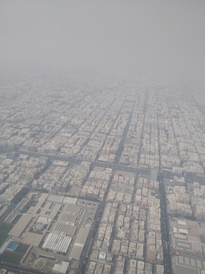 An aerial view of a densely populated urban area with a grid-like layout. The buildings are tightly packed, and the cityscape extends into the distance, fading into a hazy sky.