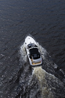 A white motorboat with a black roof cruises through dark, rippling water, leaving a foamy wake behind.