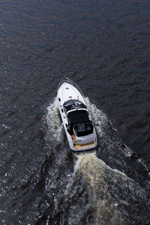 A white motorboat with a black roof cruises through dark, rippling water, leaving a foamy wake behind.