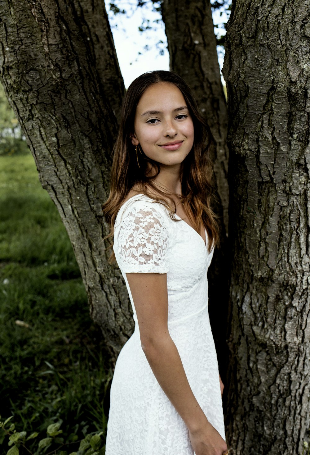 a woman in a white dress standing next to a tree