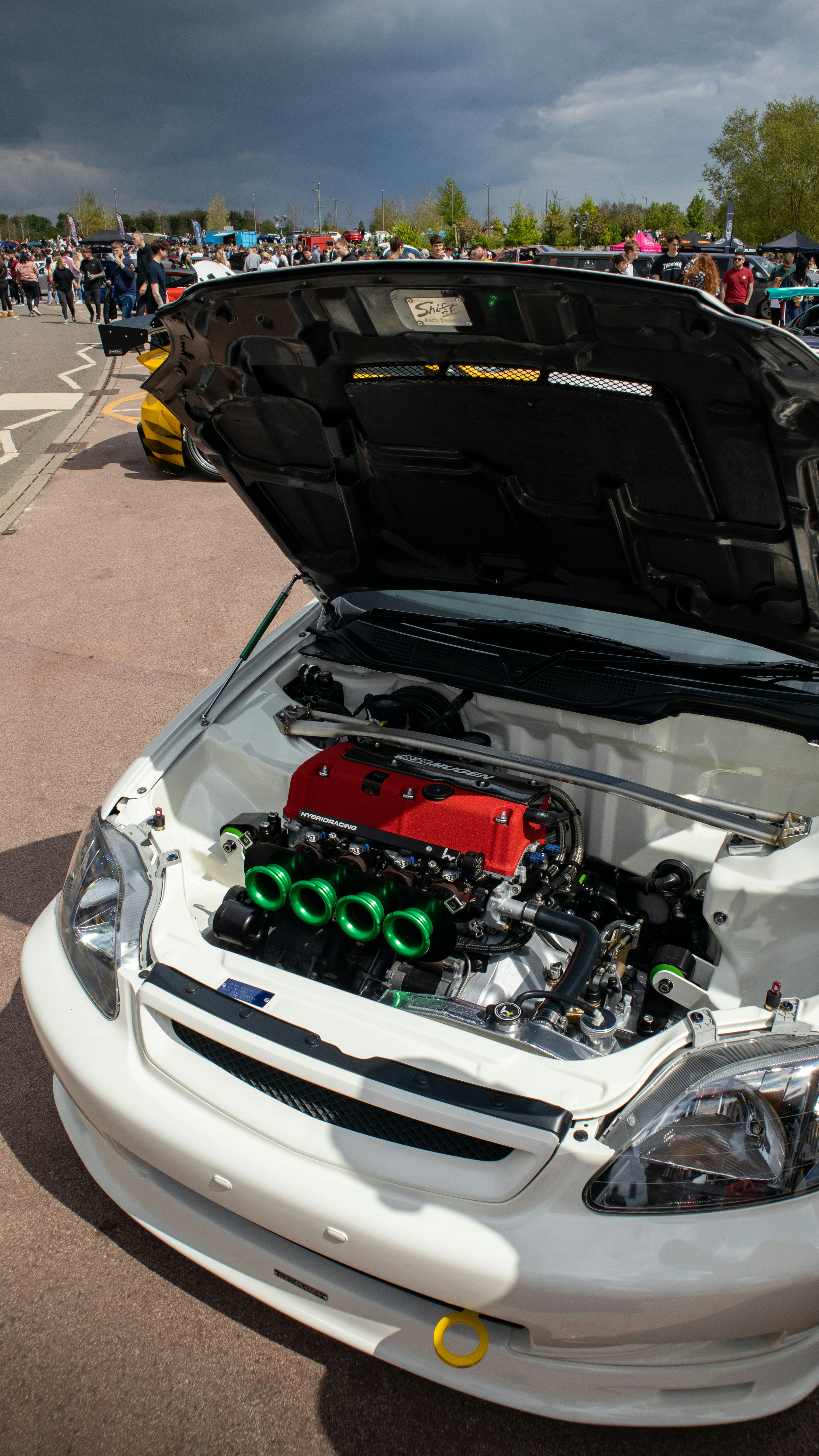 a white car with its hood open and a bunch of people around it