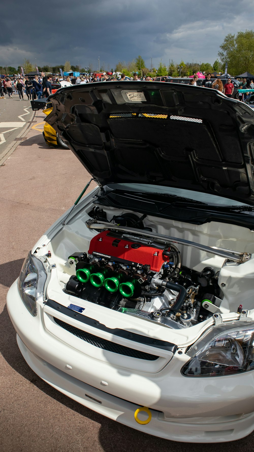 a white car with its hood open and a bunch of people around it