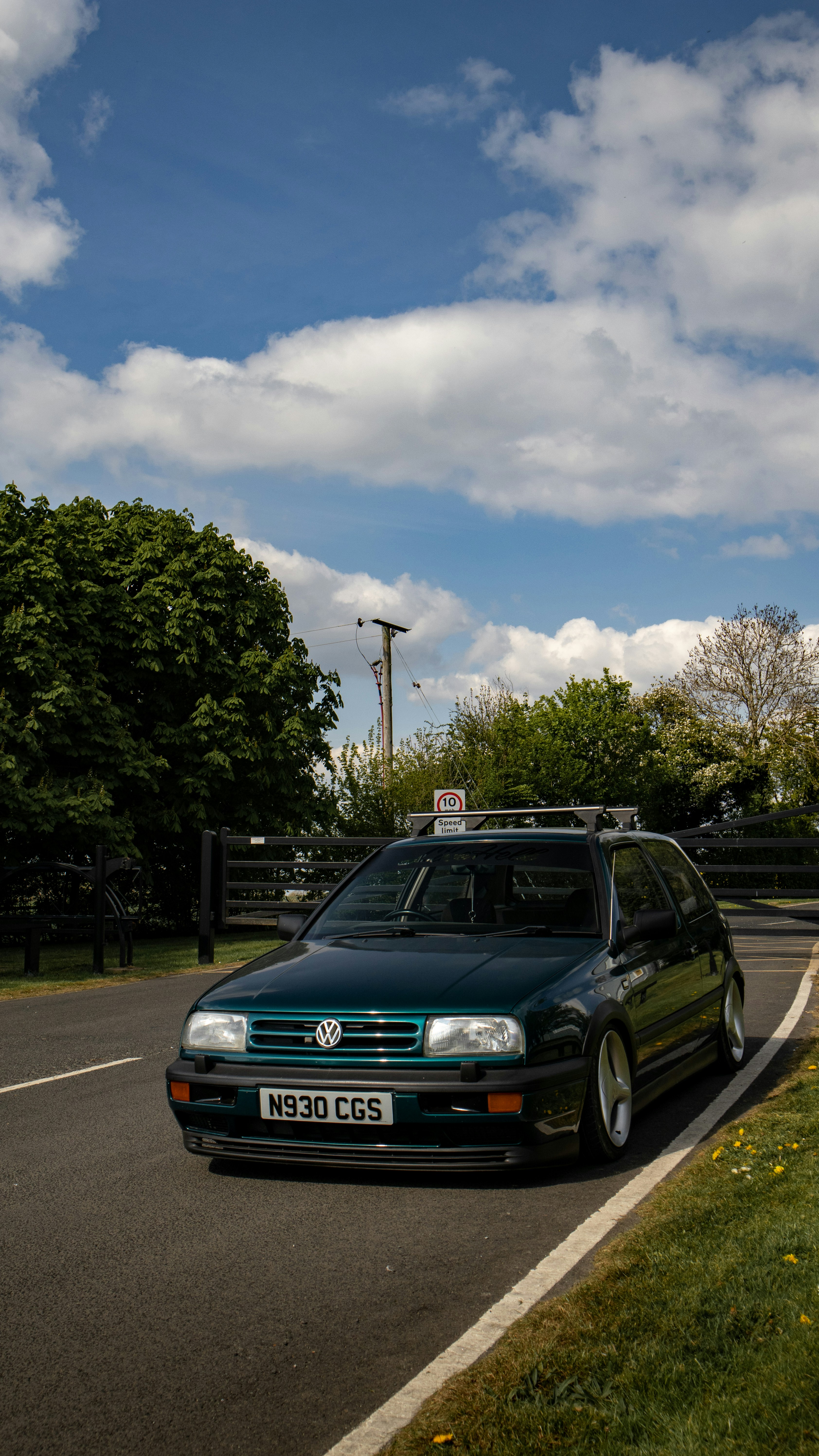 a black car driving down a street next to a lush green field