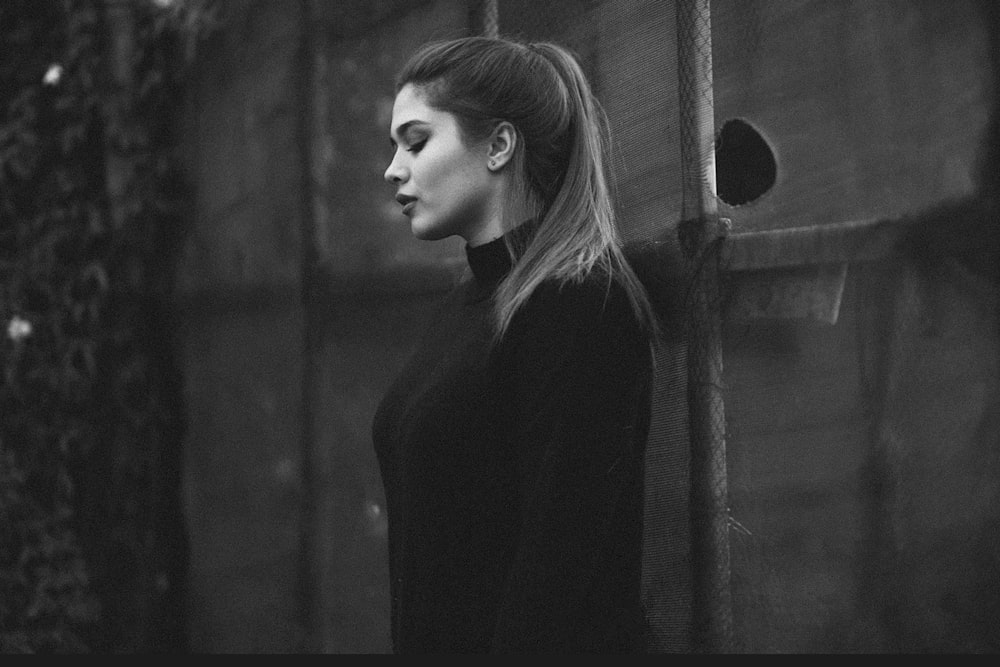 a black and white photo of a woman leaning against a wall