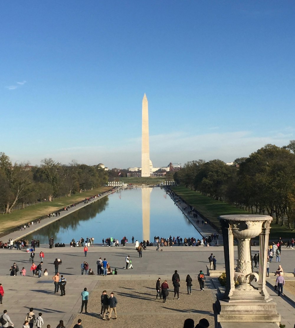 a group of people standing around a reflecting pool in the middle of a park