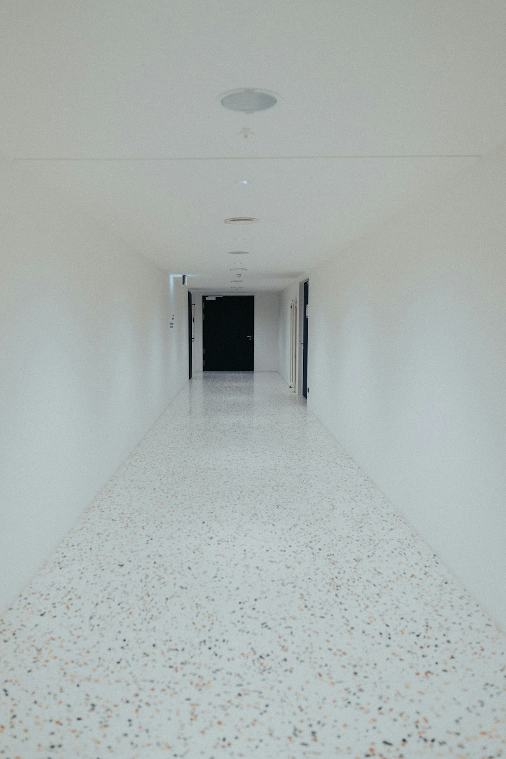 a long hallway with white walls and a black door