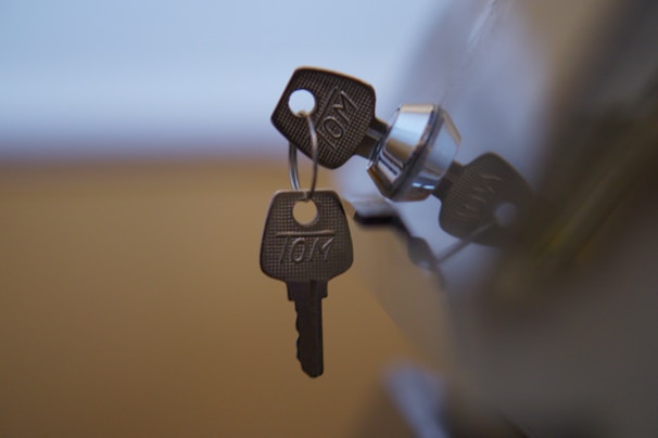 Two metal keys are hanging on a keyring, inserted into a shiny, metallic lock.