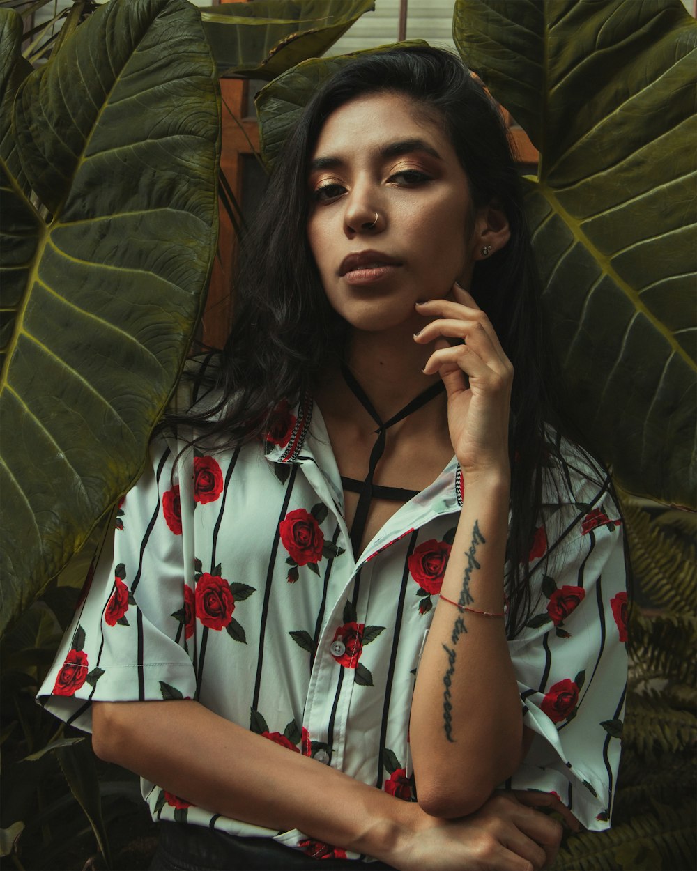 a woman with a tattoo on her arm standing in front of a plant