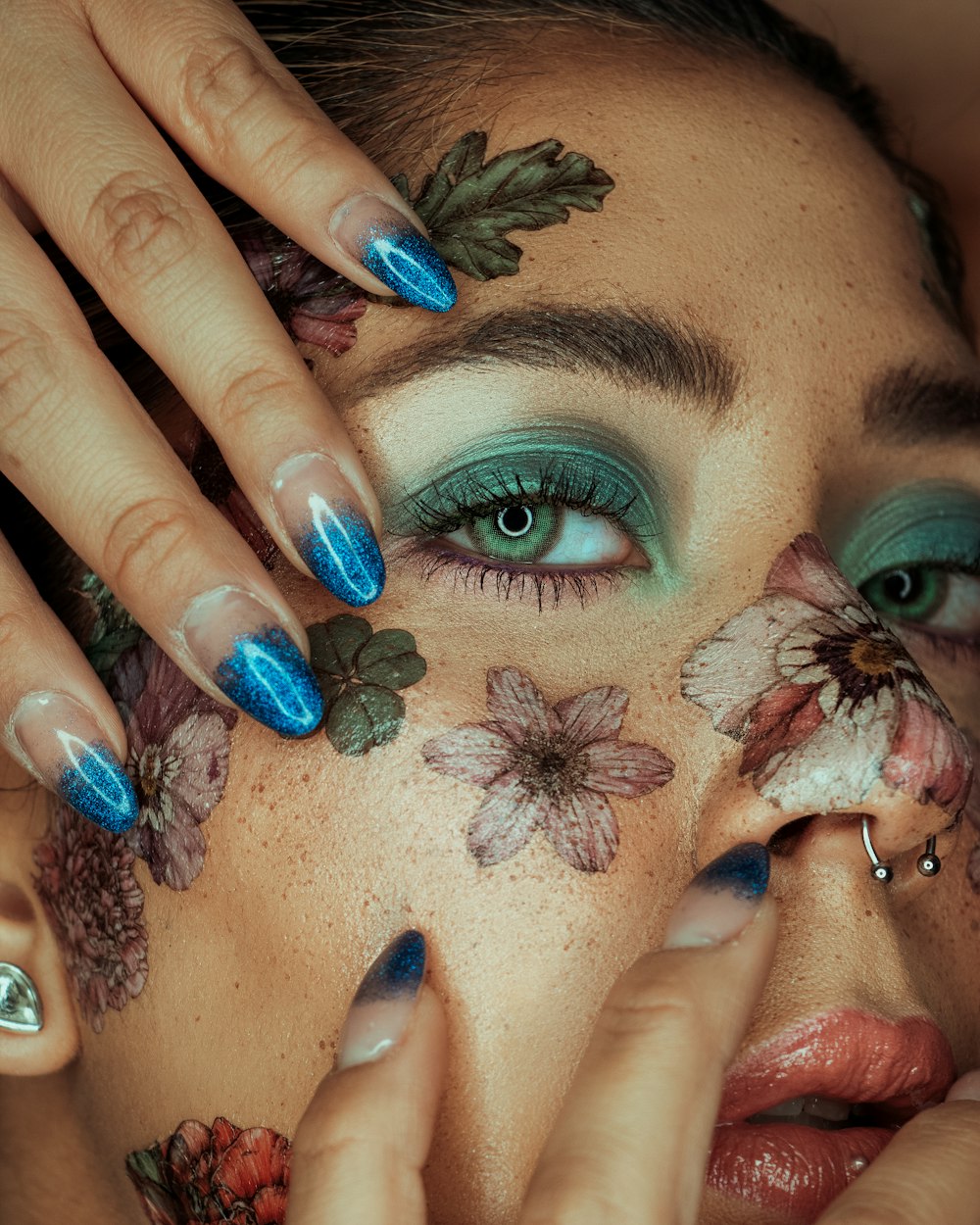 Eine Frau mit blauem und grünem Make-up und Blumen im Gesicht