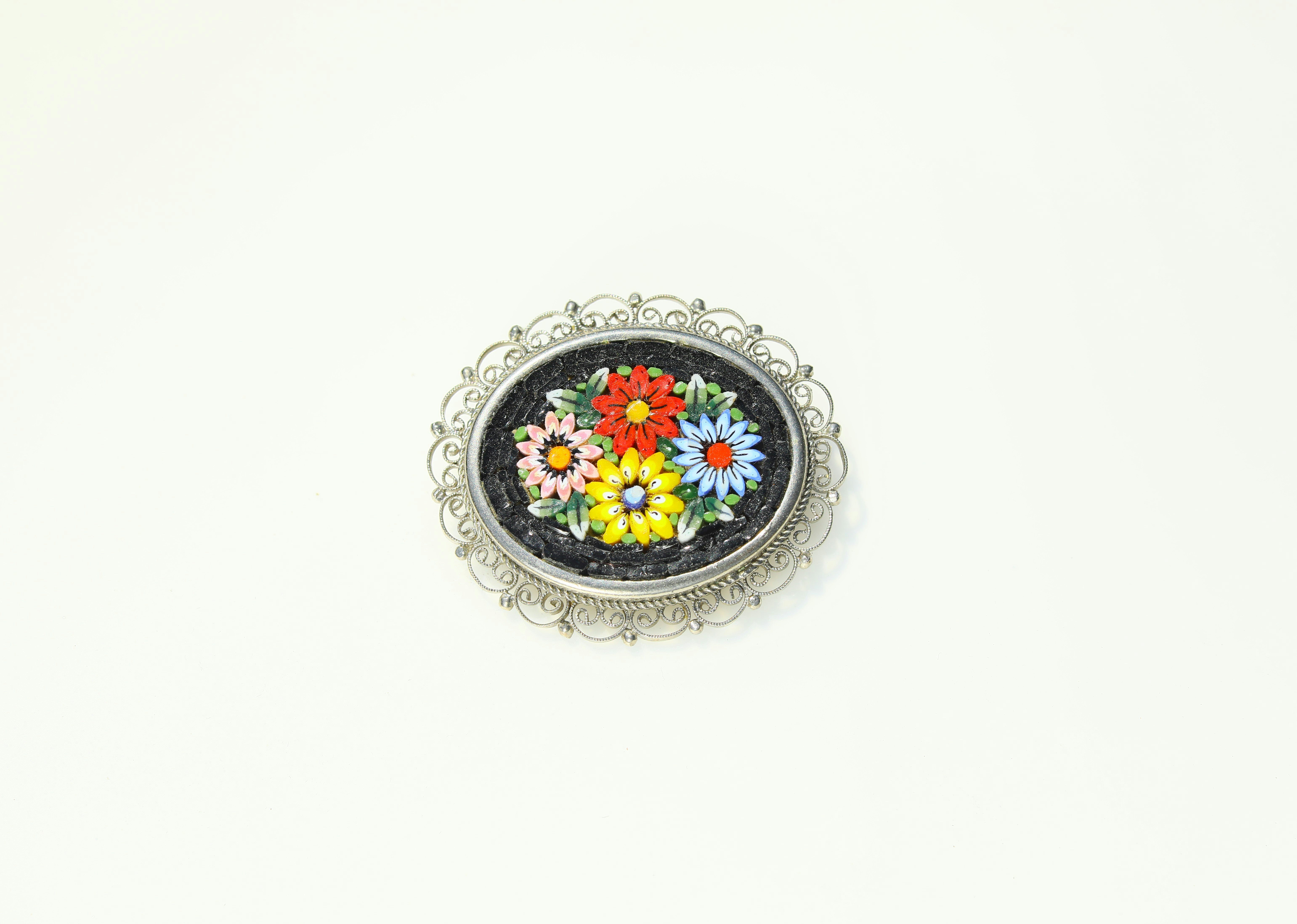 Antique silver brooch with intricate floral pattern on cream velvet background, bright studio lighting