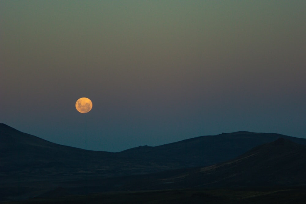 a full moon rising over a mountain range