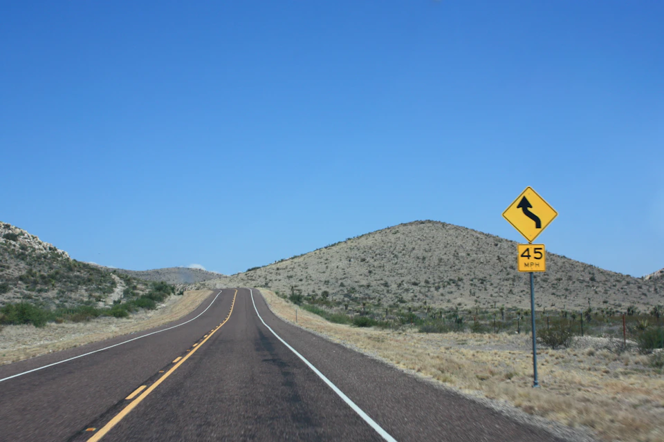 Desert road with yellow diamond-shaped sign warning drivers of sharp curve ahead nearby