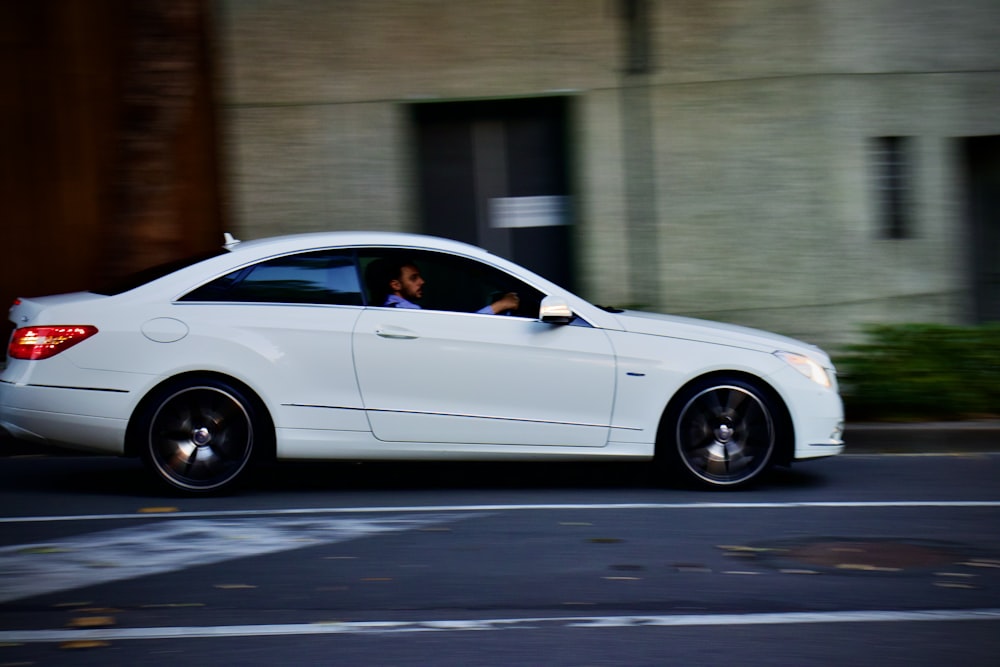 a white car driving down a street next to a tall building