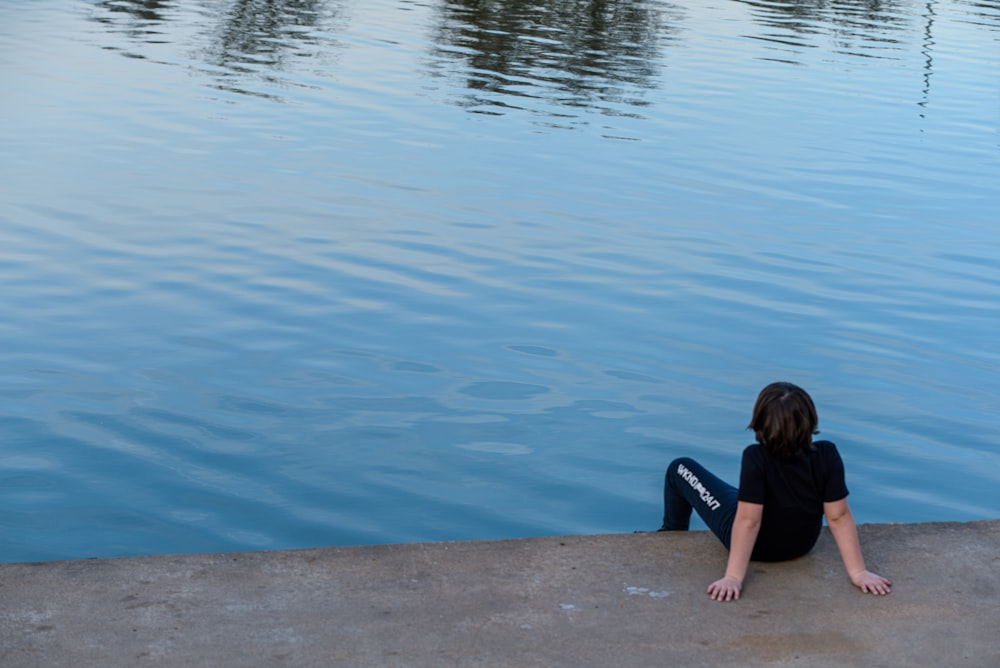 a woman sitting on the edge of a body of water