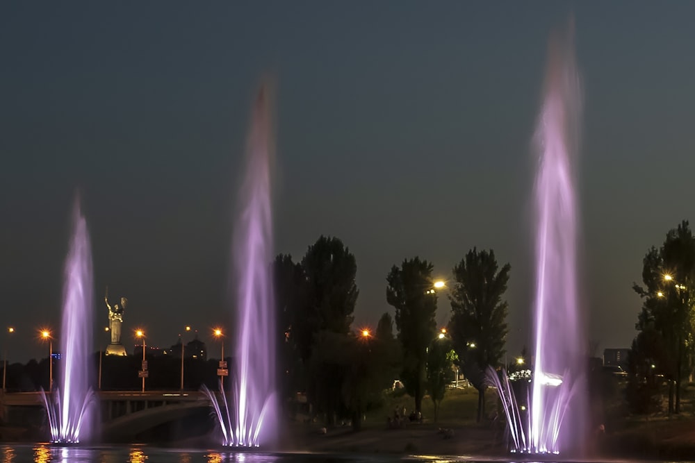 a group of water fountains lit up at night