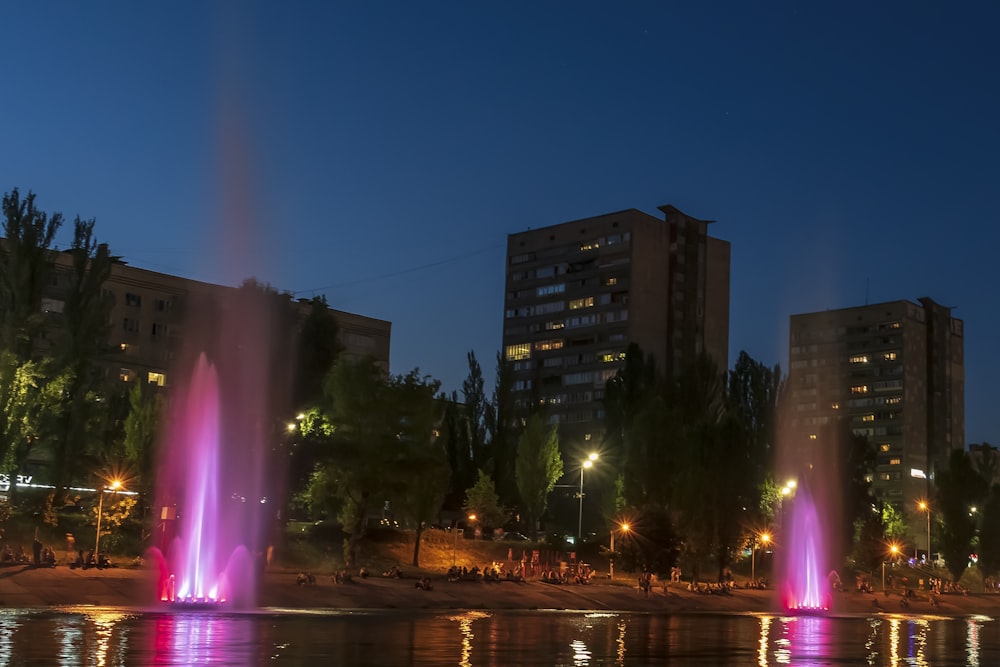 a group of water fountains in front of a city at night